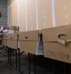 Mortician and funeral director Bryan Clayton inspects names on a row of cardboard caskets, one reading "COVID+," at Maryland Cremation Services in Millersville, Md.