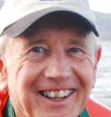 A portrait of Frederick Frey in an orange life vest standing in front of a stretch of water