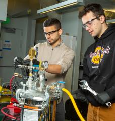 MIT engineers Aly Kombargi (left) and Niko Tsakiris (right) work on a new hydrogen reactor, designed to produce hydrogen gas by mixing aluminum pellets with seawater.