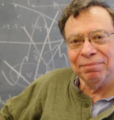 A portrait of Carl Wunsch standing in front of a blackboard with white chalk math drawings in the background.